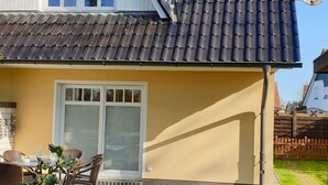 Ein Haus mit Ziegeldach, Satellitenschüssel und einer Terrasse mit Gartenmöbeln.