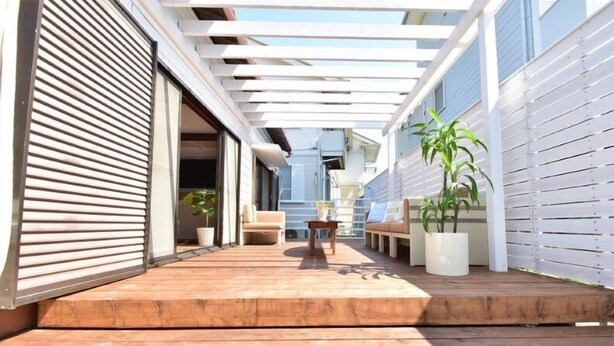 Un patio techado al aire libre con piso de madera, una zona de estar con mesa y sillas, y plantas en macetas.