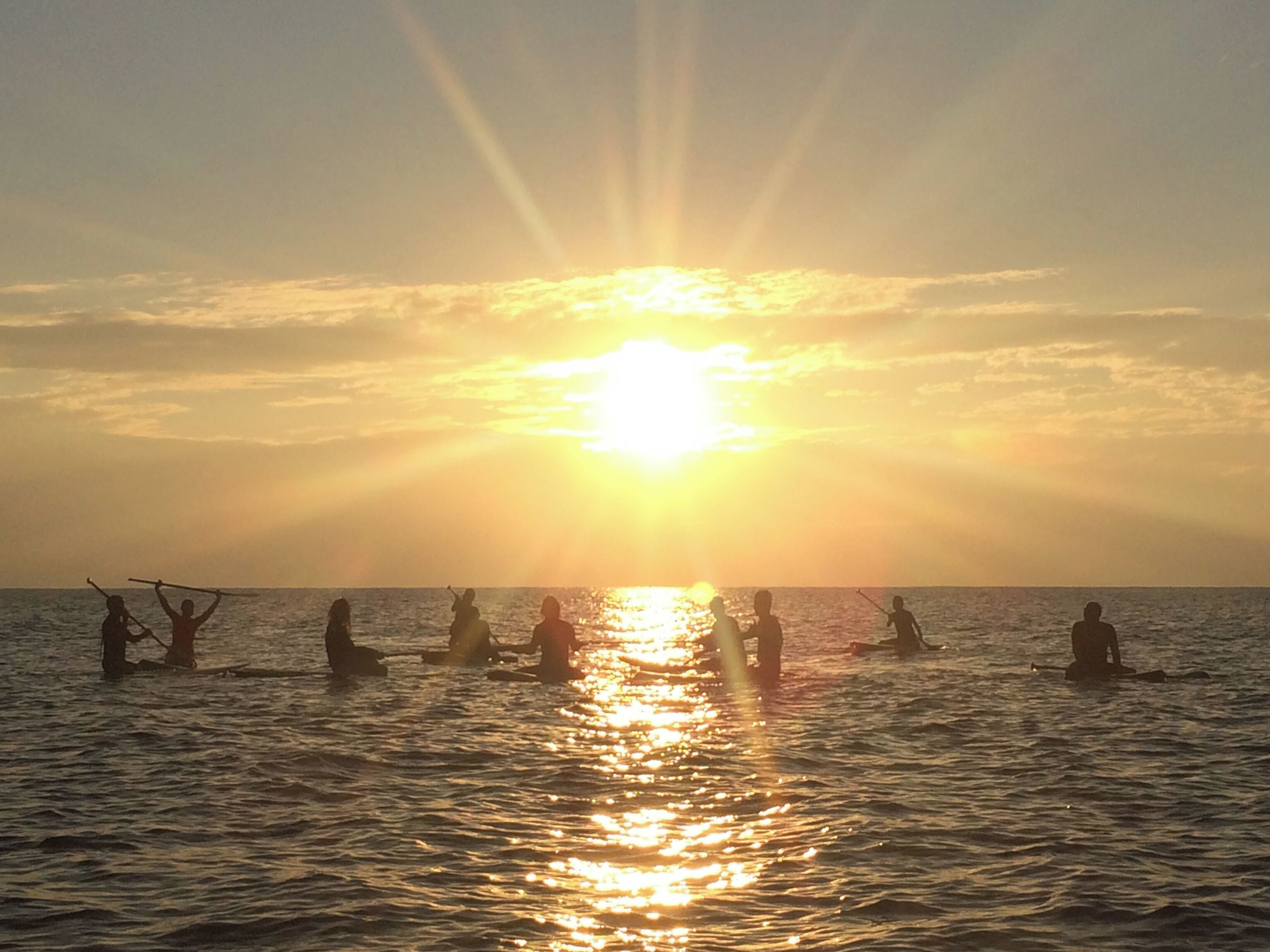 A sunset over the ocean with people in the water.