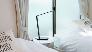 Una habitación de hotel con cama, mesita de noche con lámpara y ventana con cortinas.