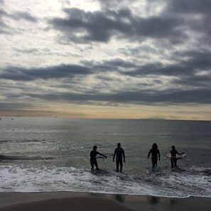 Une scène de plage où l’on voit des personnes se promener le long du rivage, certaines portant des planches de surf.