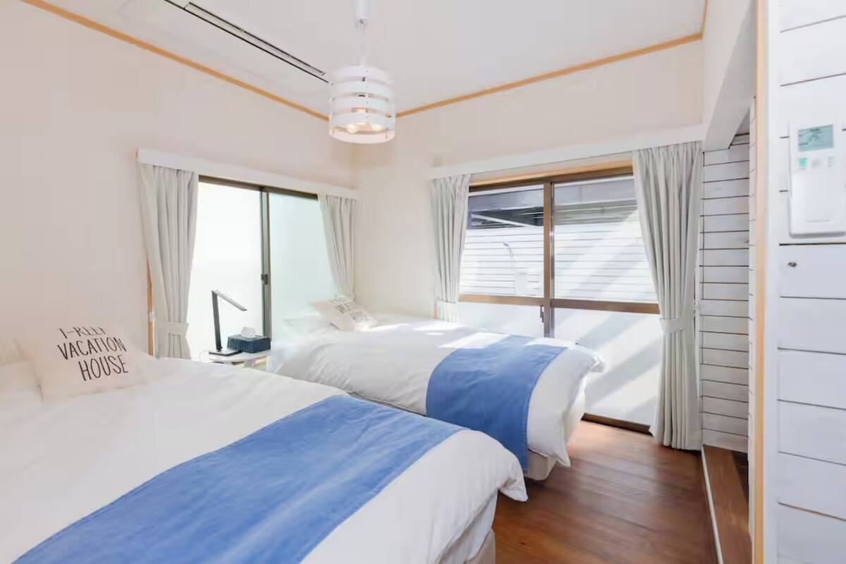 Une chambre avec deux lits, une fenêtre et un thermostat fixé au mur.
