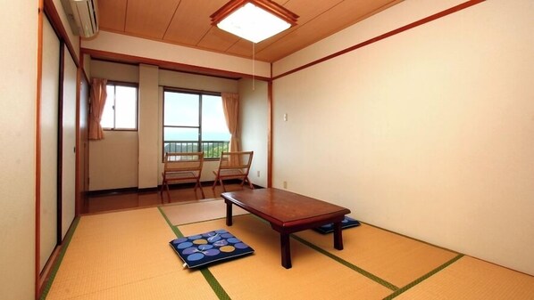 A traditional Japanese room with tatami flooring, a low wooden table, two chairs, and a view of the sea through a balcony. - Minshuku Umi no Sachi (Sasebo)