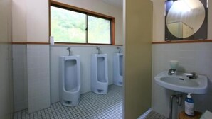 Baño de hombres con tres orinales, una ventana y un lavabo con espejo.