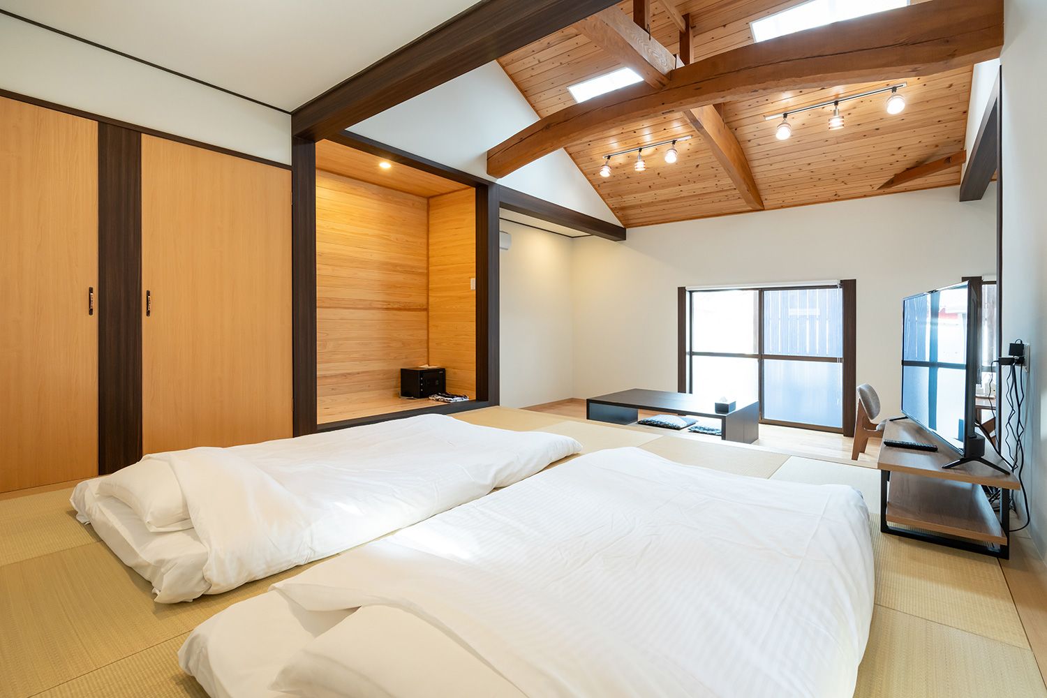 A room with two beds, a desk with a computer, and a large window.