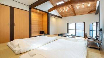 A room with two beds, a desk with a computer, and a large window.