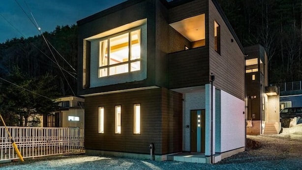 A modern two-story house with large windows and a visible interior. - Villa Fuji Bon Voyage Sora (Fujikawaguchiko)