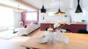 A modern living room with a wooden dining table set for a meal, a white sofa, and a pink accent wall. - Villa Fuji Bon Voyage Sora (Fujikawaguchiko)