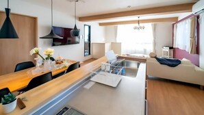 A modern kitchen with a central island, dining area, and a living space with a sofa and a TV. - Villa Fuji Bon Voyage Sora (Fujikawaguchiko)