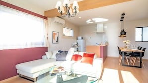 A modern living room with a glass coffee table, a white sofa, and a dining area with a wooden table and chairs. - Villa Fuji Bon Voyage Sora (Fujikawaguchiko)