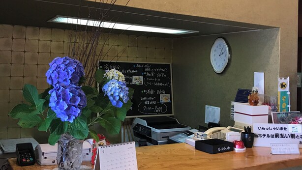 En receptionsdisk med en klocka, en menytavla och en vas med blommor.
