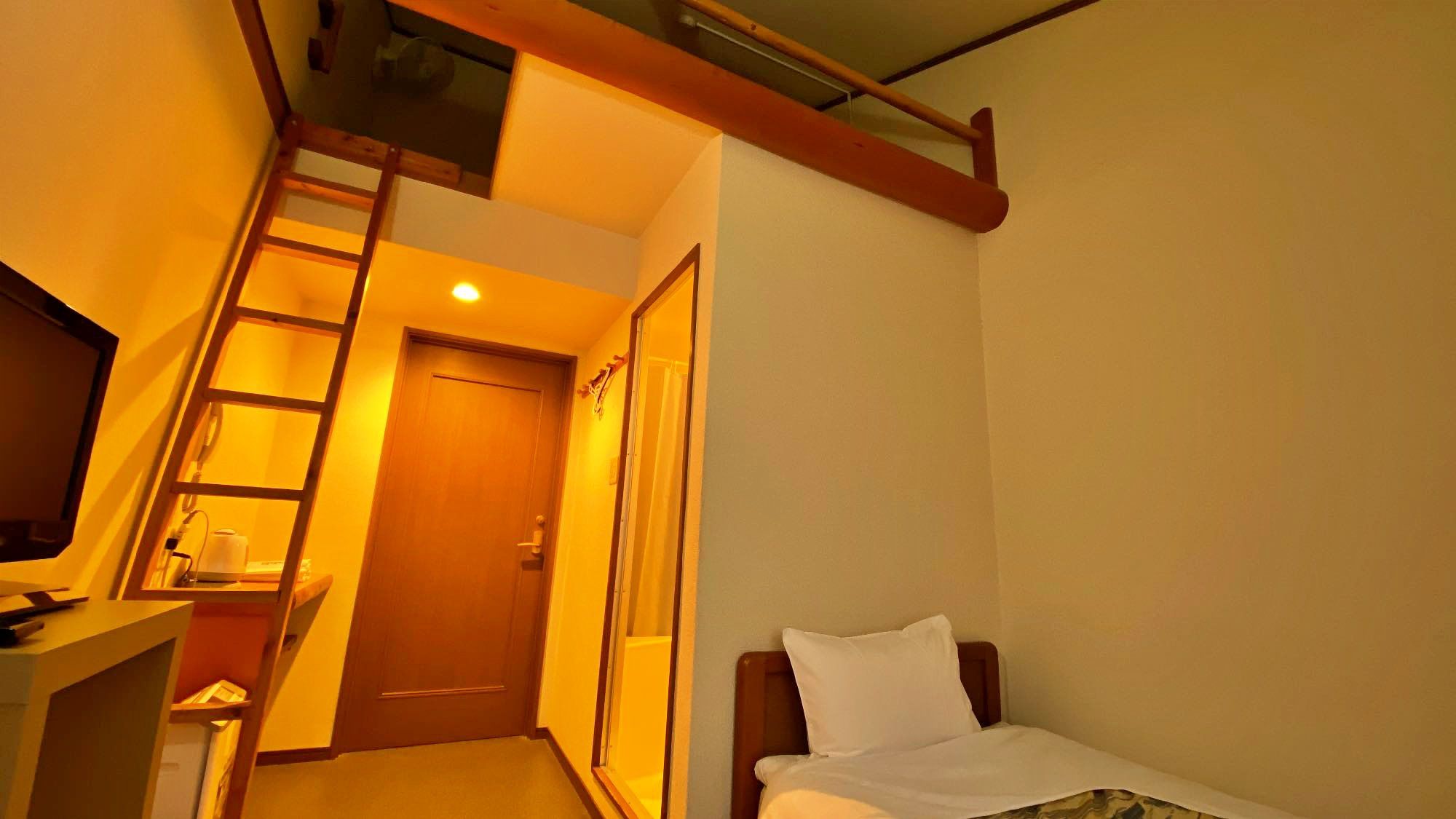 Habitación de hotel compacta con cama, escritorio y una escalera que da a un balcón.