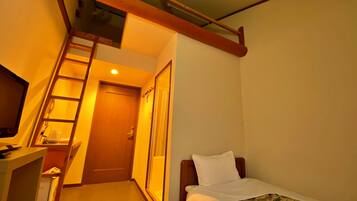 Habitación de hotel compacta con cama, escritorio y una escalera que da a un balcón.