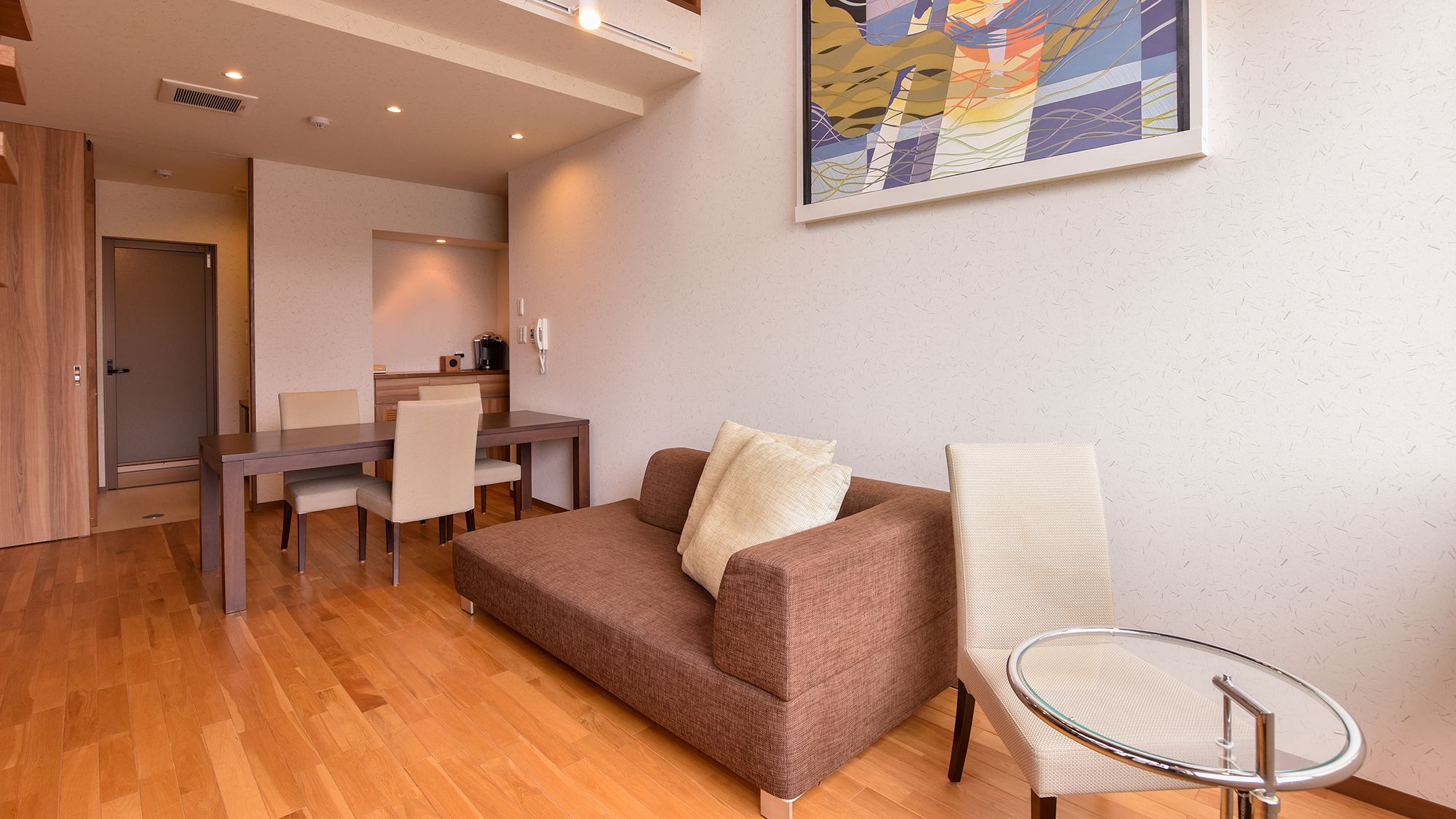 Una sala moderna con un sofá marrón, una mesa de vidrio y una zona de comedor con una mesa y sillas de madera.