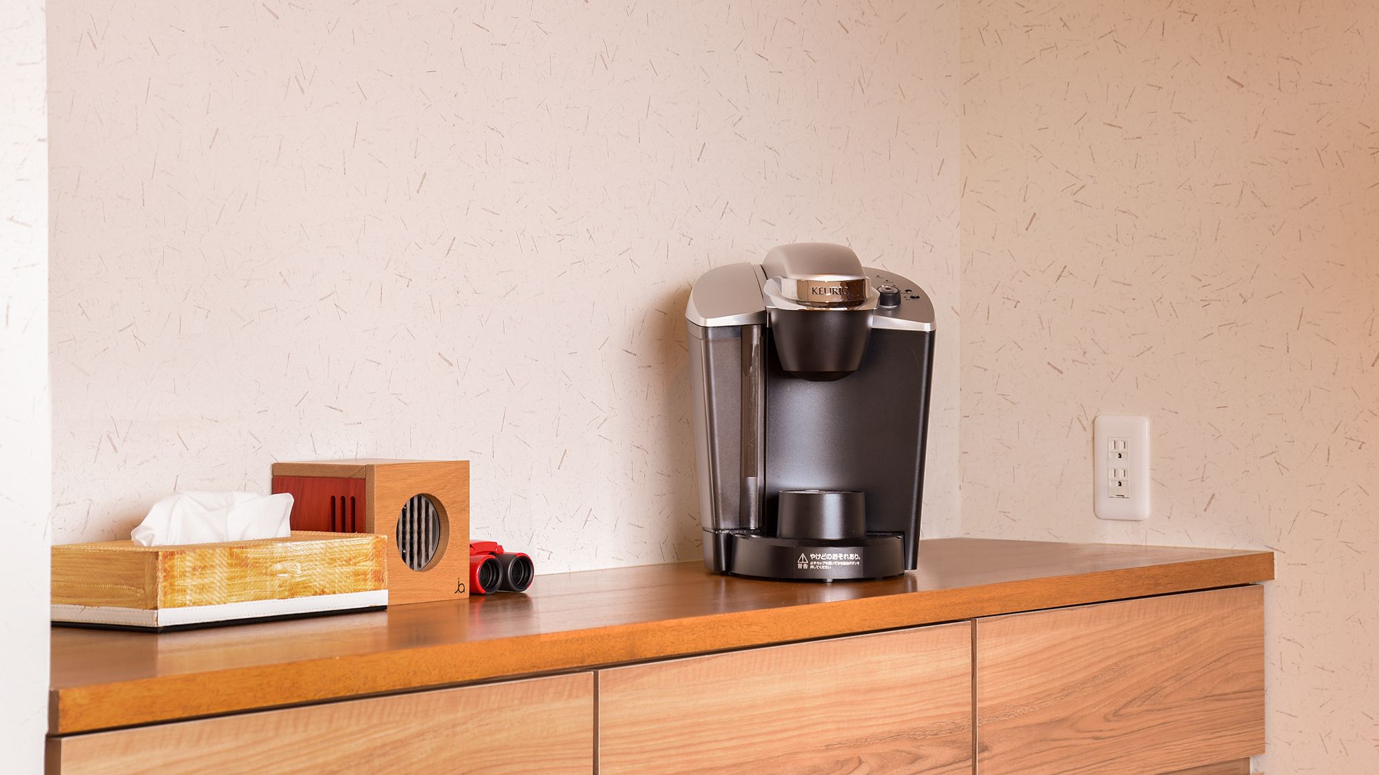 Una cafetera sobre una encimera de madera, con una caja y unos binoculares a un lado.