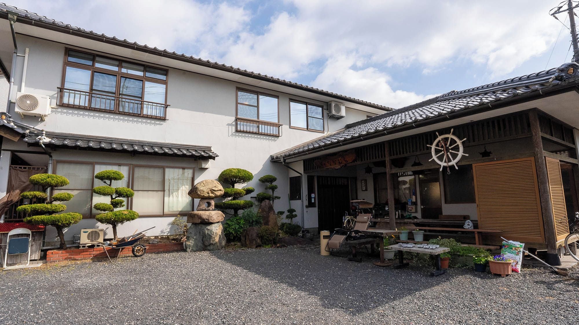 En traditionell japansk byggnad med en täckt uteservering, en stenlykta och välansade bonsaiträd.