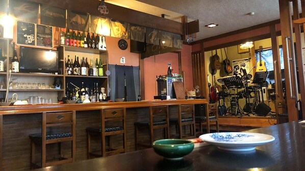 A bar area with wooden stools, shelves of bottles, and a green bowl on the counter. - Otomaridokoro Nakamura <oki Shoto> (Ama)