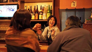 Un bar con un televisor mostrando un programa, estantes llenos de botellas y un letrero con caracteres japoneses.
