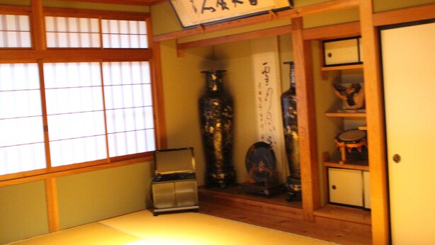 Une pièce de style japonais traditionnel, avec un sol recouvert de tatamis, un paravent en papier de riz (shoji) et une étagère en bois où sont disposés divers objets.