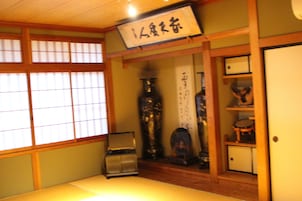 Una habitación japonesa tradicional con suelo de tatami, un separador shoji y una estantería de madera con diversos objetos.