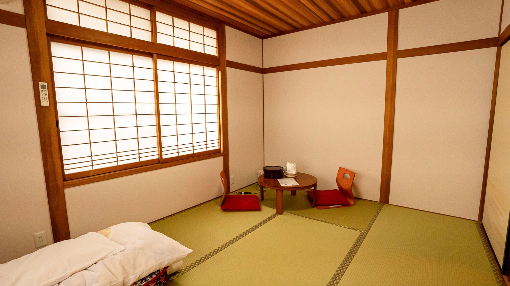 A traditional Japanese room with tatami flooring, a low table with a kettle, and two chairs.