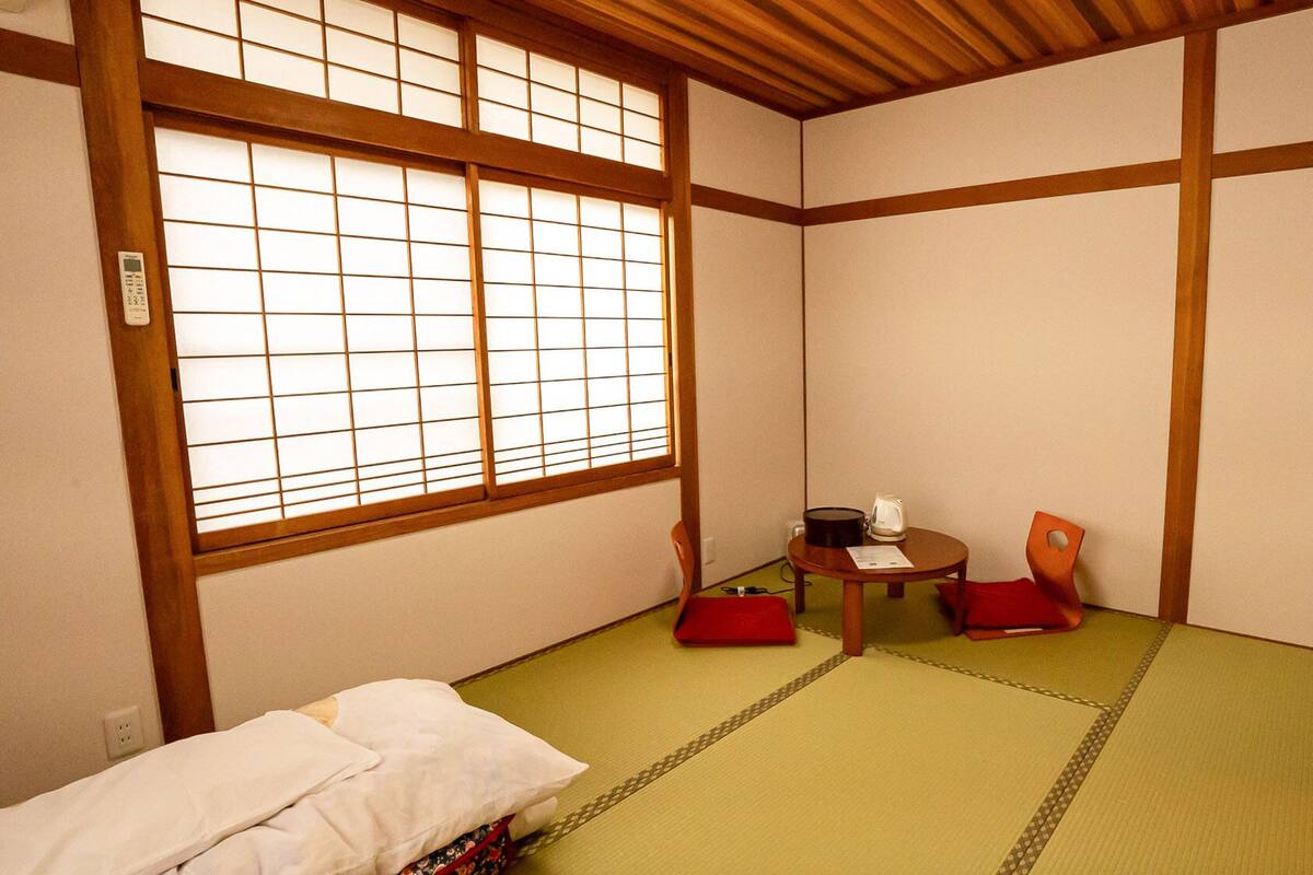 Una habitación japonesa tradicional con suelo de tatami, una mesa baja con un hervidor y dos sillas.