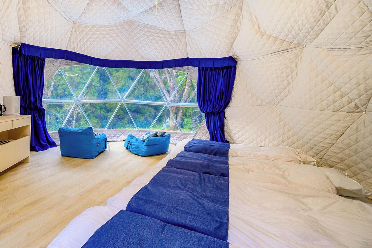 A tent-style room with a large window, a bed, a blue sofa, and a wooden floor.