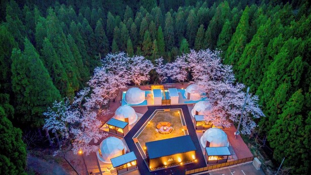 An aerial view of a resort with multiple dome-shaped structures, surrounded by a forested area and a parking lot. - Rupo no Mori (Fukui)