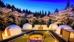 A resort with geodesic dome structures, a central fire pit area, and cherry blossom trees. - Rupo no Mori (Fukui)
