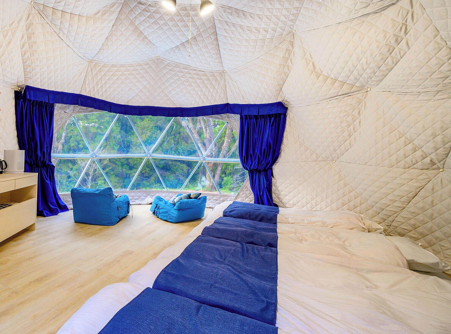 Habitación tipo tienda de campaña con un ventanal grande, una cama, un sofá azul y suelo de madera.