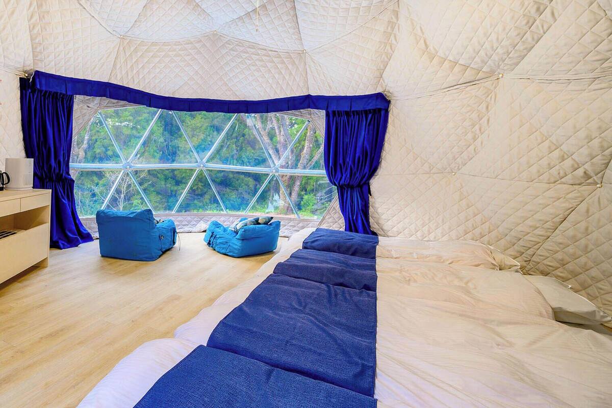 A tent-style room with a large window, a bed, a blue sofa, and a wooden floor.