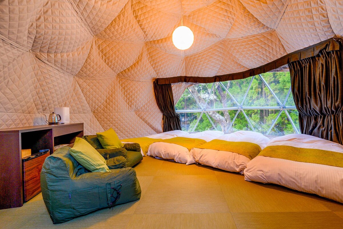 A cozy, dome-shaped room with a bed, pillows, a bean bag, and a small table with a kettle.