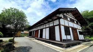 Un edificio tradicional japonés con fachada de madera y tejado de tejas, que cuenta con un porche cubierto y un camino de piedra que conduce a la entrada.