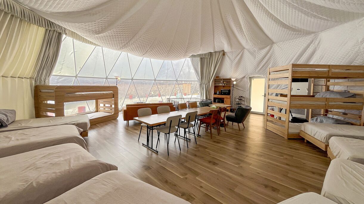 A tent-style room with bunk beds, a dining table, chairs, and a view through large windows.