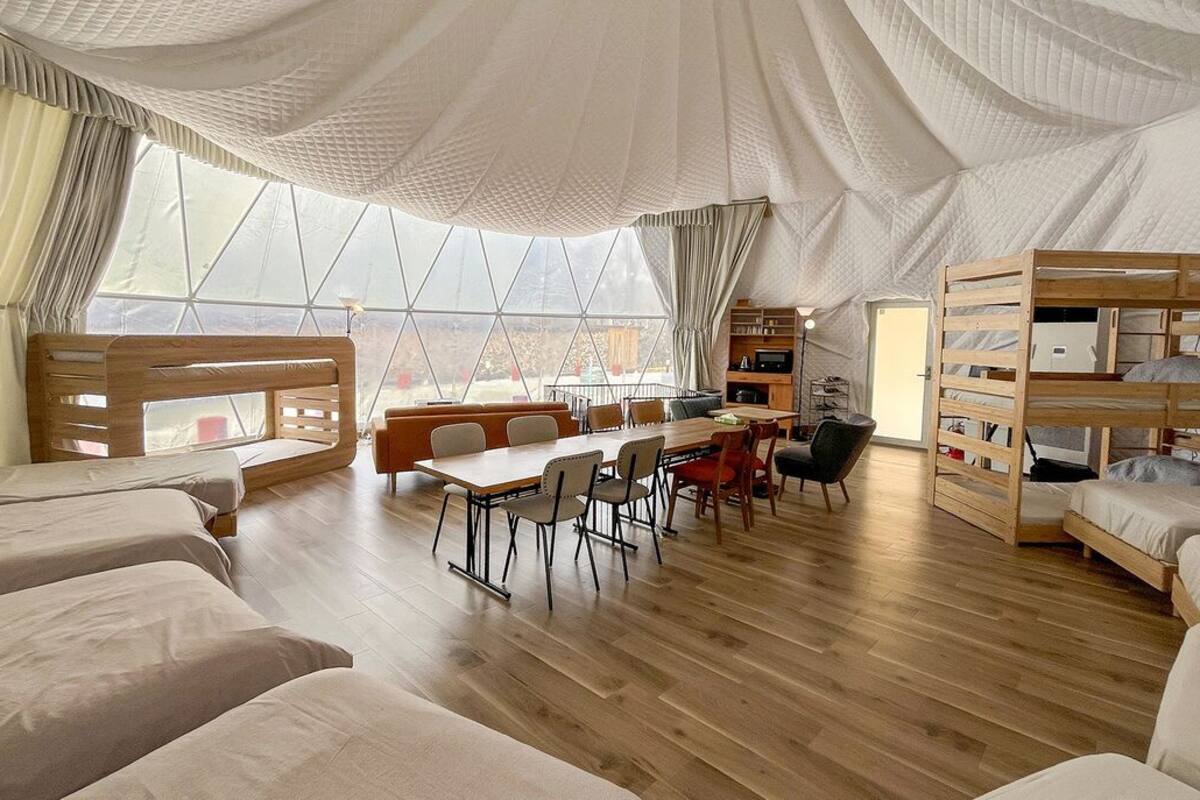 A tent-style room with bunk beds, a dining table, chairs, and a view through large windows.