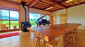 Una habitación amplia con una gran mesa de madera, un piano y una estufa de leña.