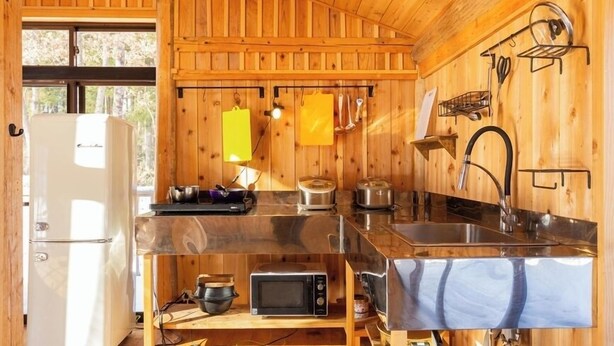 Una cocina compacta con paredes de madera, un lavamanos de acero inoxidable, un microondas y una estufa.