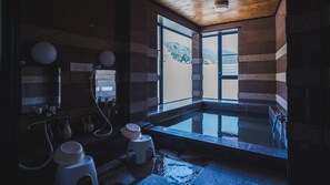A traditional Japanese onsen with a stone bath, wooden ceiling, and a view of a mountain. - Takiyoshi Guesthouse (Tanabe)