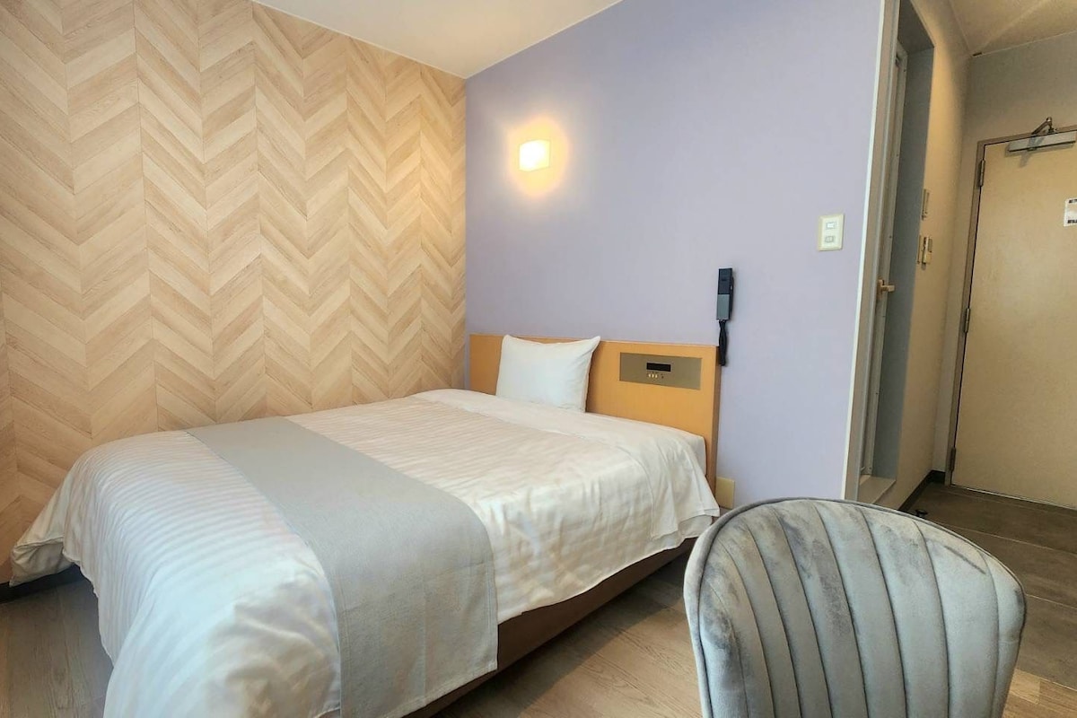 Een hotelkamer met een bed, een stoel, een aan de muur bevestigd telefoon en een deur.