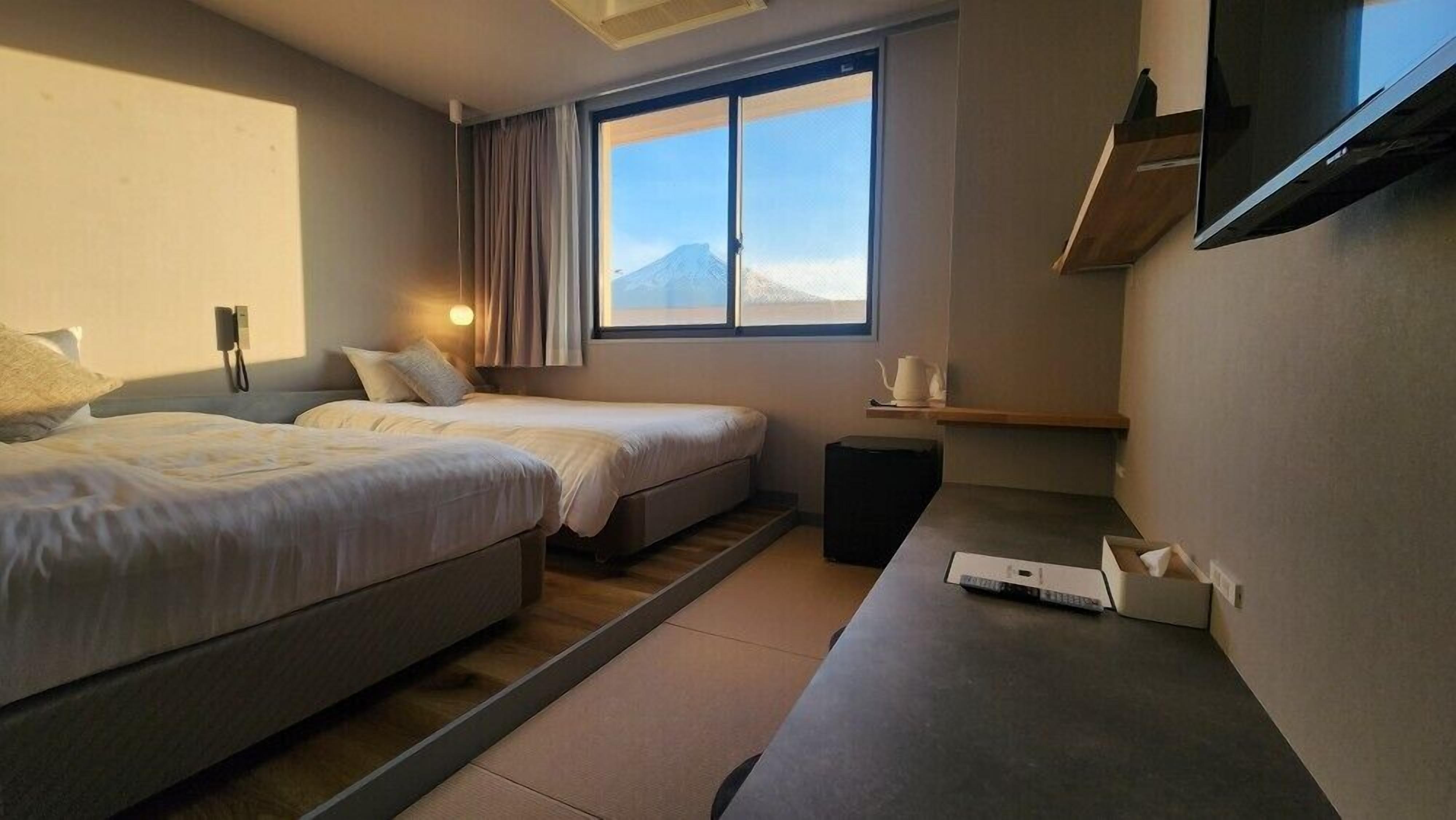 A hotel room with two beds, a desk, a TV, and a window with a mountain view.