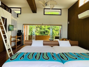 Ein Schlafzimmer mit einem großen Bett, einem Fernseher, einer Leiter und Blick auf Grün durch eine Schiebetür.