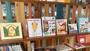 Una estantería con libros infantiles, una manta de ganchillo y un taburete de madera.