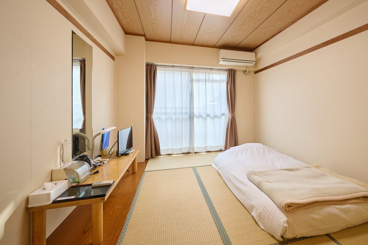 Una habitación de hotel con cama, escritorio con computadora, espejo y aire acondicionado.