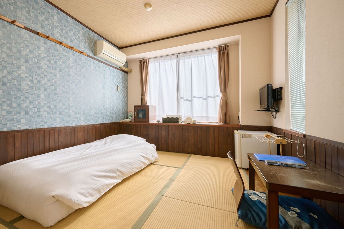 A room with a bed, a desk, a TV, and a window with curtains.