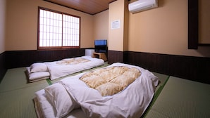 A traditional Japanese-style room with tatami mat flooring, two single beds with white bedding, a television on a wooden stand, and a large window with wooden frames. - Business Hotel Wayokan/annex Wako (Inazawa)