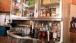 A bar area with a refrigerator stocked with beverages, a selection of liquor bottles, and a counter with glasses and bottles. - The giraffes cottages restaurant and bar (Nairobi)