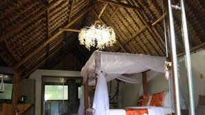 A room with a four-poster bed, a wooden floor, a red carpet, and a thatched roof. - The giraffes cottages restaurant and bar (Nairobi)