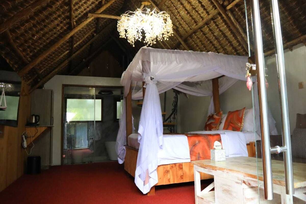Ein Zimmer mit einem Himmelbett, Holzboden, rotem Teppich und einem Strohdach.