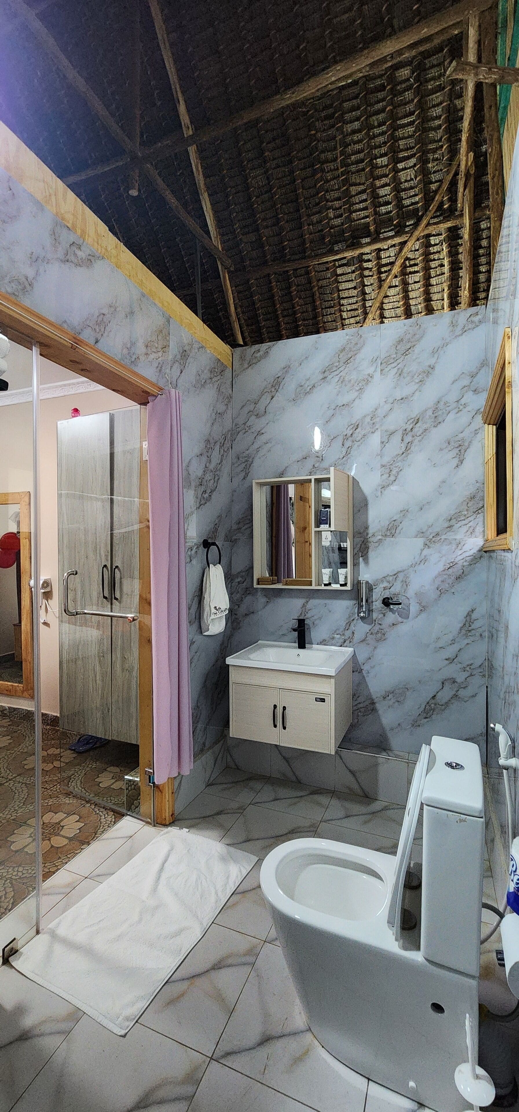 Une salle de bain avec un mur en marbre, un lavabo, des toilettes et un espace douche.