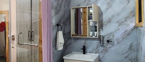 Une salle de bain avec un mur en marbre, un lavabo, des toilettes et un espace douche.